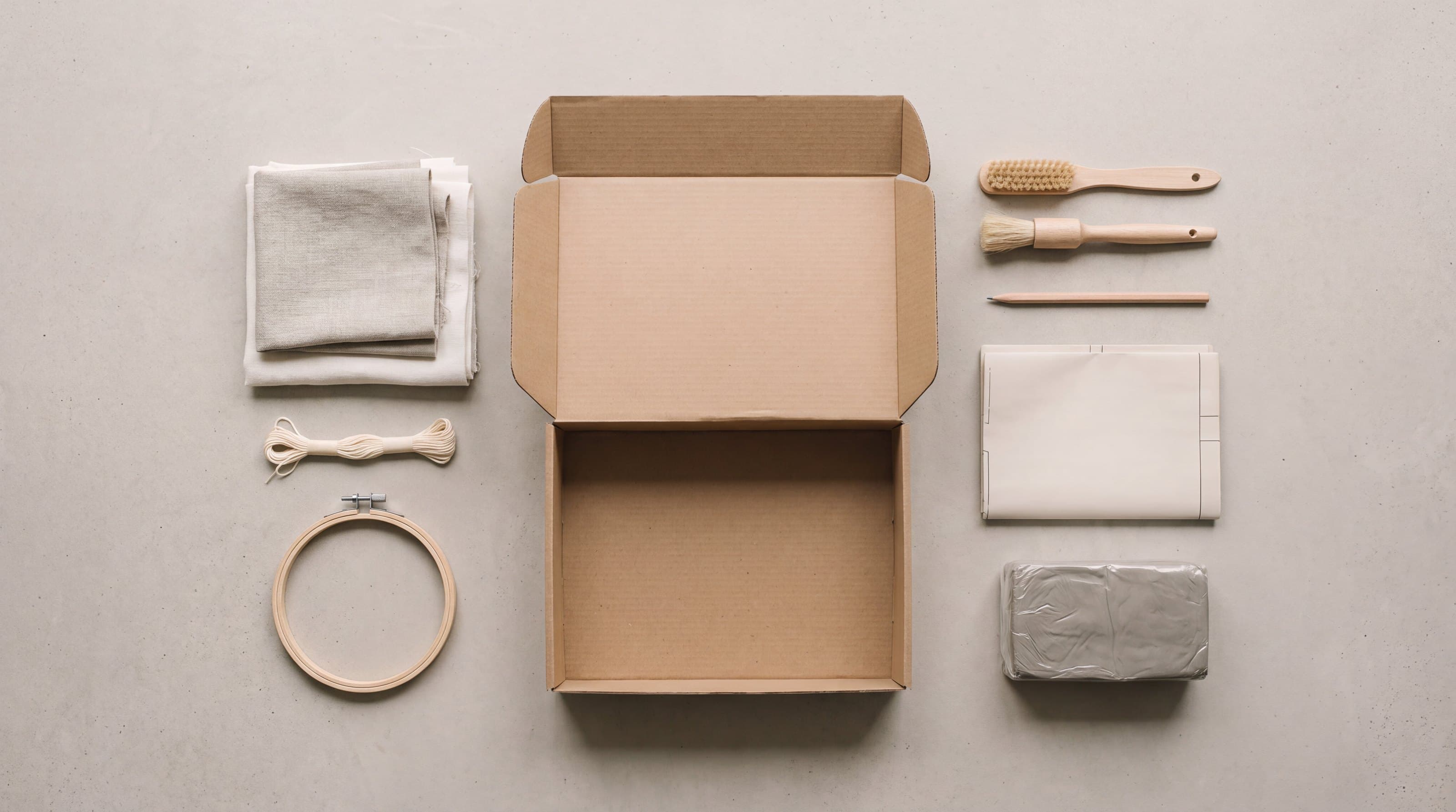 A materials kit laid out flat: fabric swatches, thread, brushes, pattern paper and clay